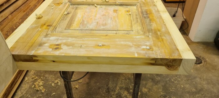 Gamla dörrar som byggmaterial för en sänggavel, förstärkt och breddad på arbetsbänk i snickeriverkstad.