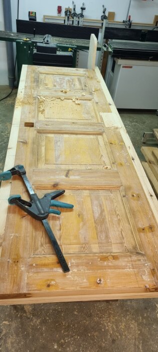 Gammal dörr i trä bearbetas för att bli en sänggavel, med en stor tving fastsatt på den.