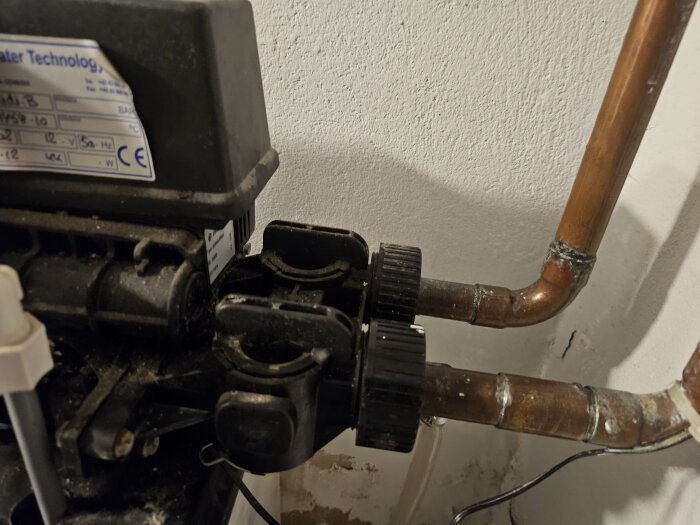 Kopparrör med vattenkopplingar intill äldre avhärdningsfilter; potentiell läcka vid en anslutning med plastmutter.