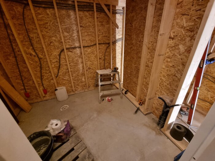 Ovanvåning under byggnation med uppreglade träväggar, verktyg, stege och virke synliga. Trångt mellanutrymme vid trappa och badrum.