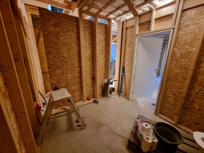 Renovering: Nyreglade väggar på ovanvåning, stege med ritning, öppen dörr till annat rum, byggmaterial på golvet.