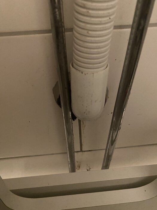 Avloppsrör under vask med två metallrör bredvid, väggmontering syns.