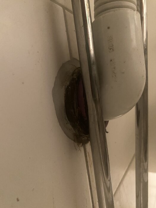 Avloppsrör under badrumsvask med droppande vatten där röret går in i väggen, omgiven av två metallstänger.