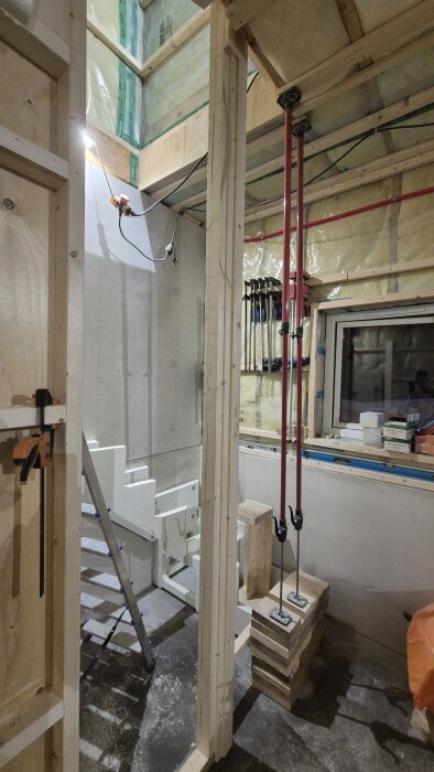 Provmonterad stolpe i trä under trappbygge, omgiven av verktyg och material i en pågående renoveringsmiljö.