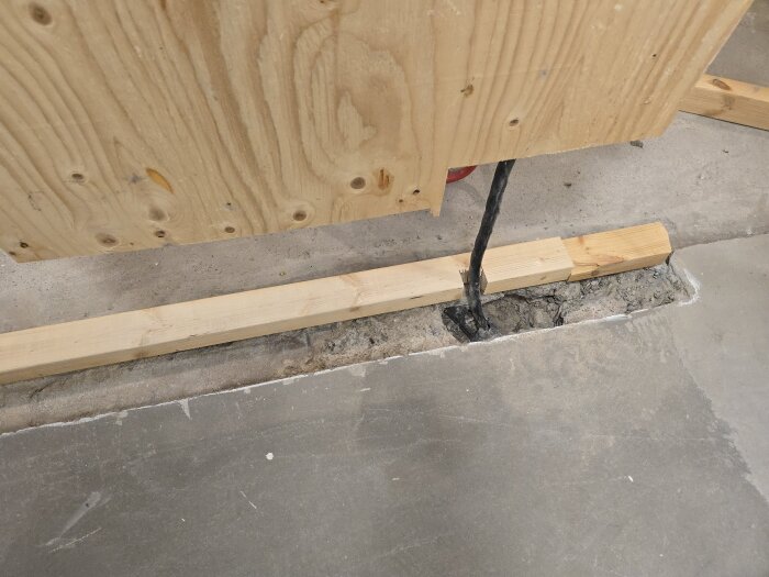 Form för betonggjutning i golv, med träskivor och brädor, elsladdar som sticker upp genom betongen, redo för vidare arbete.