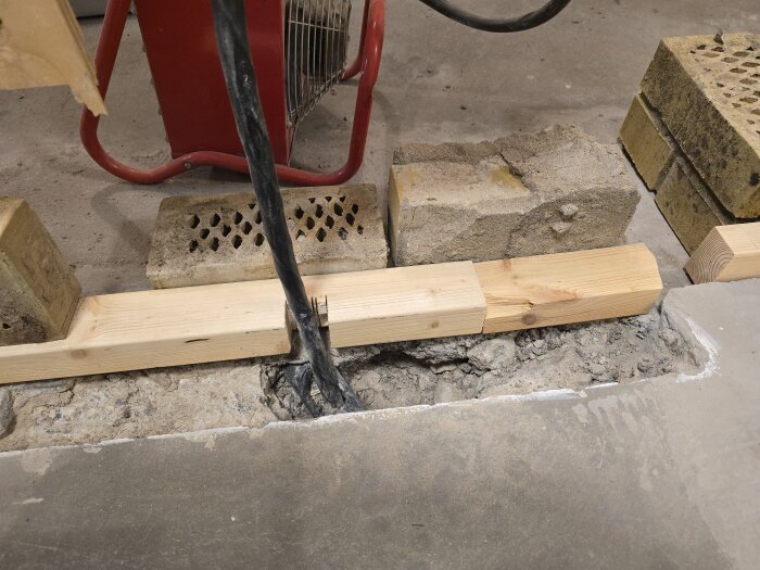 Formarbete med träplankor och tegelstenar vid en betongränna, med kablar synliga, förbereds för att gjuta en innervägg.