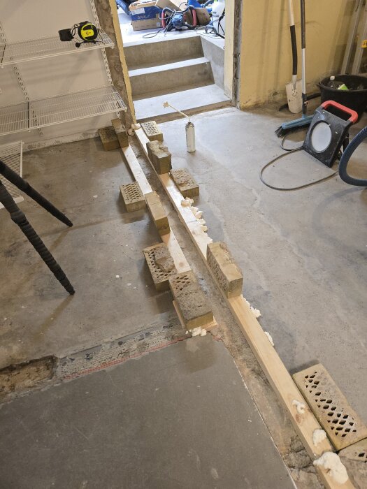 Form för betonggjutning i en ränna, omgiven av tegelstenar som håller den på plats. Verktyg och utrustning ses i bakgrunden.