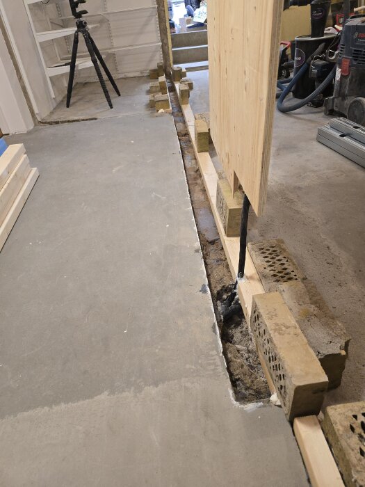 Formbyggnad för innervägg med tegelstenar, träskivor och synlig kabelkanal i ett renoveringsprojekt. Kamera och verktyg i bakgrunden.