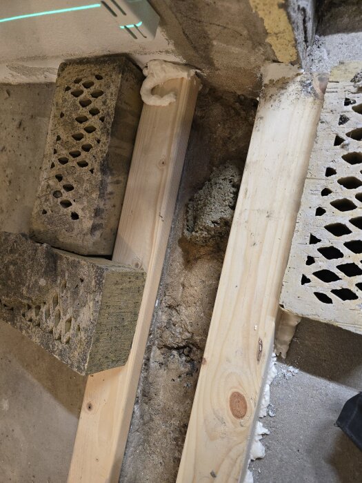 Tegelstenar håller formvirke på plats, omgivna av fogskum för förankring. Laserlinje synlig på betongväggen för höjdjustering.