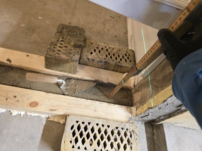 Mäta höjden för betonggjutning av innervägg, form och laser används. Tegelstenar stabiliserar formen, spackelverktyg synligt.