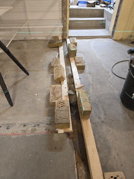 Träform för gjutning av betong i en ränna, hålls på plats med tegelstenar. Laser används för att kontrollera höjd och precision.