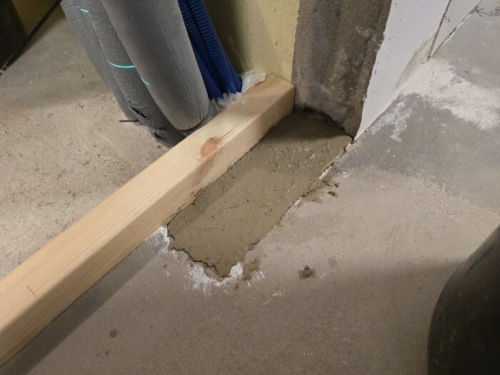 Formvirke och betong i ränna på golvet, med elrör ovanpå, hålls på plats av en träribba. Betongen är nyligen lagd och ser jämn ut.