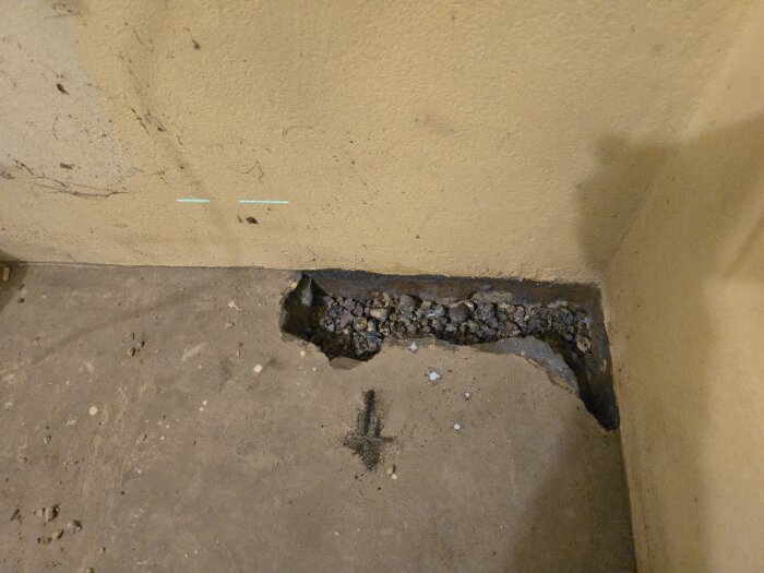 Ränna i betonggolv fylld med grus, omgiven av väggar med laserlinjer för höjdjustering inför betonggjutning.