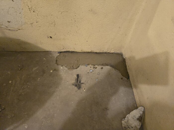 En slät betongyta i ett hörn på ett golv, med färsk betong lagd runt en öppning; väggarnas bas visar rester av arbete.