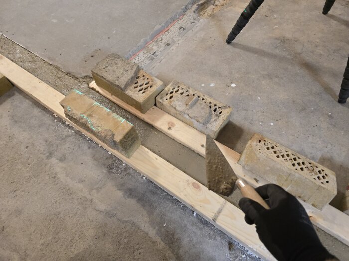 Tegelstenar och en murarslev på en golvyta med nylagt betong, trall används som form vid renovering av innervägg.