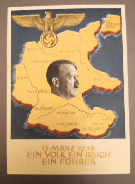 Vykort från 1938 med karta över Tyskland och profil av man. Text: "13. März 1938, Ein Volk, Ein Reich, Ein Führer", och örn med symbol.