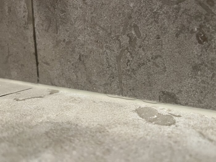 Vatten på golv och ändrad färg i fog längs vägg i dusch, tecken på läckage eller bristfällig tätning.