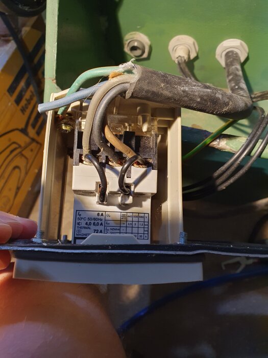 Motorskyddsbrytare med synliga kablar och specifikationer inuti en bordssåg, delvis öppet hölje.