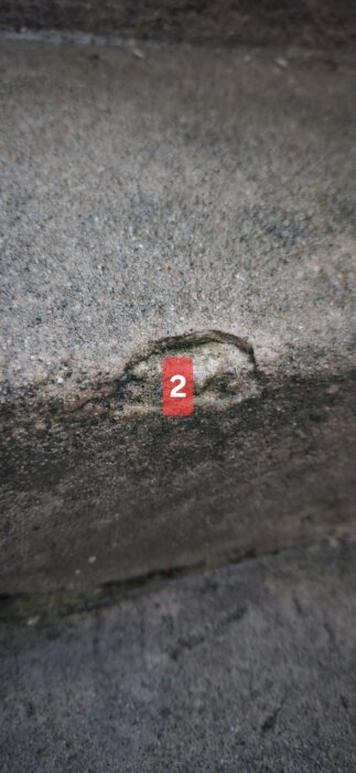 Trappsteg i betong med synlig sliten yta och mindre urgröpning, markerad med nummer 2.