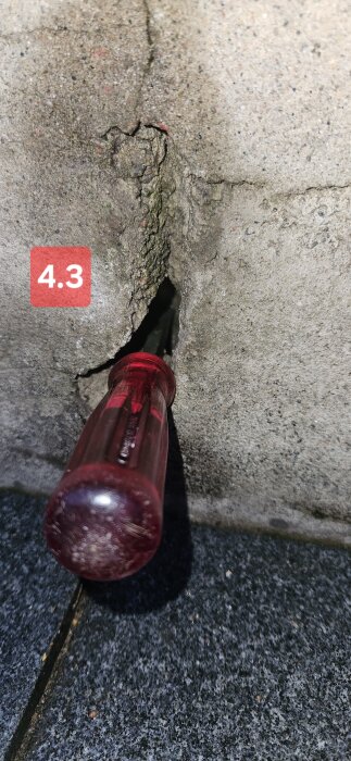 Spricka i vägg av lecablock med en röd skruvmejsel instucken i sprickan, märkning "4.3" i rött i övre vänstra hörnet.