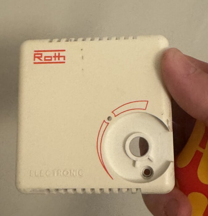 En gammal Roth-termostat med en justeringsvridknapp och hand som håller termostaten.