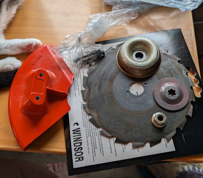 Rund sågklinga i metall med diverse tillbehör och ett rött klingskydd på ett bord.