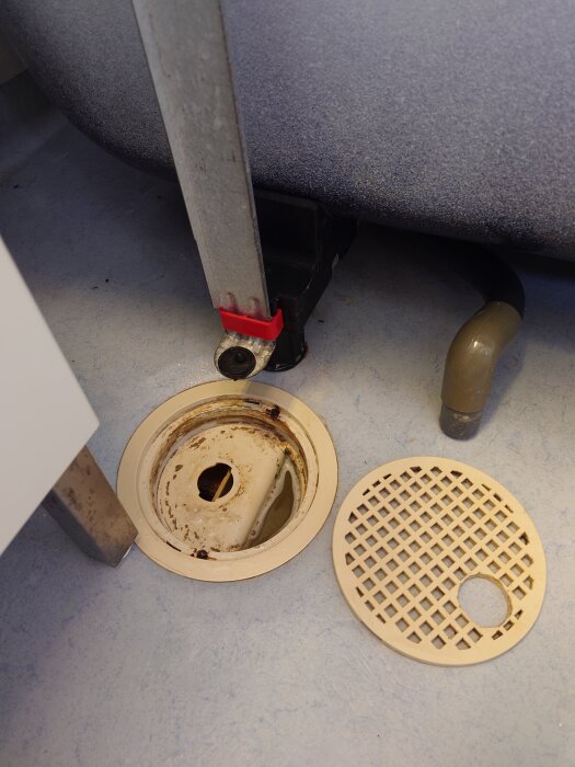 Golvbrunn från 1990 utan lock, metallstång och plastgaller bredvid.