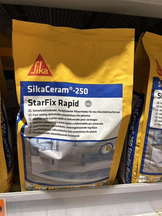 Paket med SikaCeram-250 StarFix Rapid, cementbaserad fästmassa för plattor, på en hylla i butik.