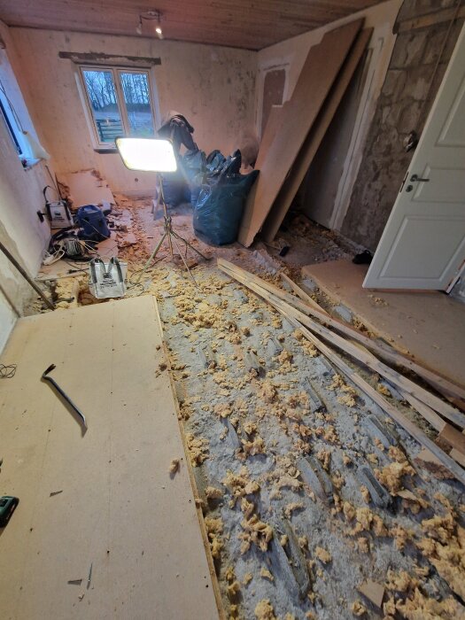 Renovering av sovrum med borttagna golvskivor, synlig fukt och mögelrester. Spotlight och verktyg syns bland byggmaterial.