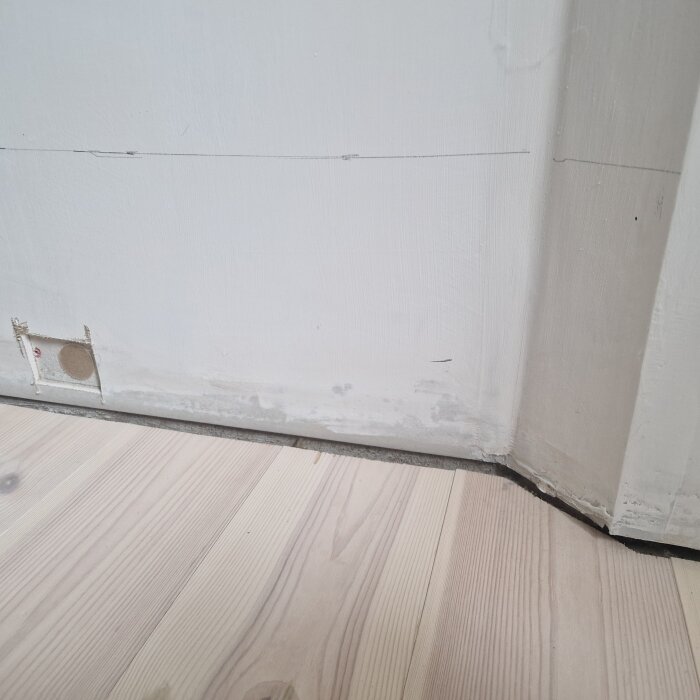 Mögliga nederdelen av en vitmålad gipsskiva vid golv i sovrum, med synliga märken där vägg möter ljust trägolv. Skadan är långs nedre delen.