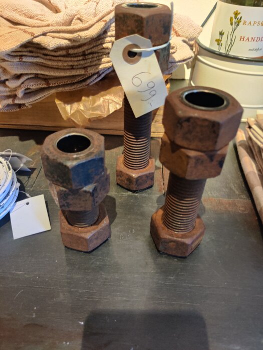 Rostiga muttrar och gängstång arrangerade som ljusstakar med prislapp i inredningsbutik.