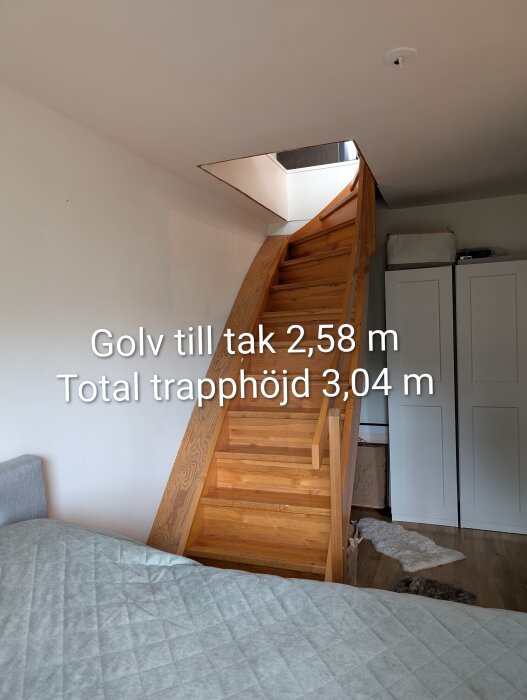 Trätrappa leder till övervåning genom smalt bjälklagshål, golv till takhöjd 2,58 m. Möbler och förvaringslådor bredvid i sovrumsmiljö.