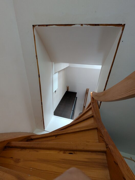 Existerande trätrappa i spiralform på övervåningen, synlig genom ett smalare bjälklagshål i betong.