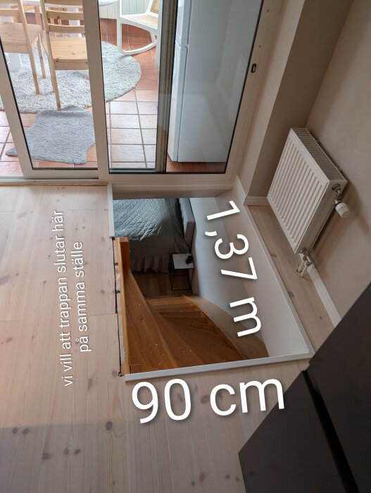 Överblick av öppning för trappa i betongbjälklag, mått 137 x 90 cm. Visar trätrappa nedan och möblerat rum genom glasdörr, med radiator till höger.