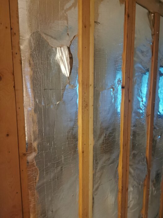 Isolering med reflekterande folie mellan träreglar, skadad och delvis trasig, utan synliga märkningar.
