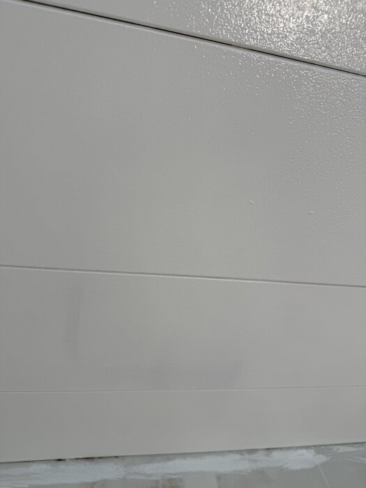 Tak med flammig målning på gipstakplattor i vardagsrum, synliga märken där färgen inte täckt korrekt.