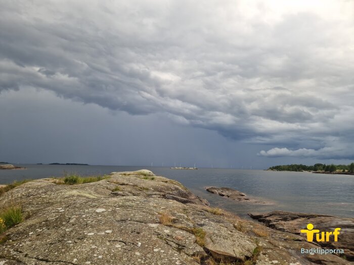 Olycksbådande himmel med mörka moln över ett kustlandskap och klippor vid havet.