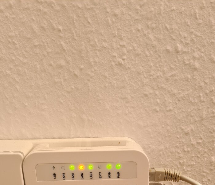 Fiberenhet med flera lysdioder som lyser, inklusive LAN och WAN-portindikatorer, ansluten med en Ethernet-kabel.