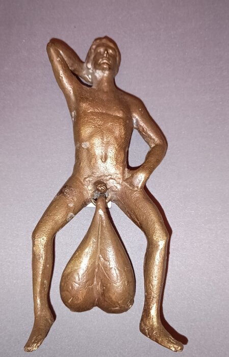 En antikinspirerad dörrkläpp i brons föreställande en stående figur med stora proportioner.