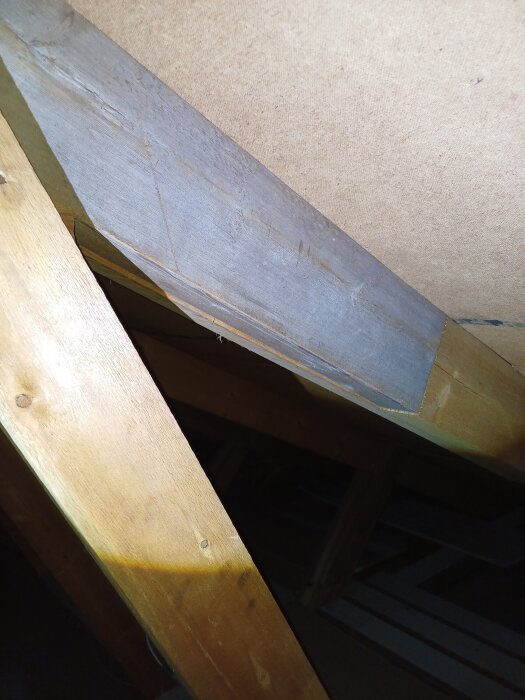 Träbalk på vind med mörka vattenfläckar, troligtvis från tidigare varningssignaler om läckage.