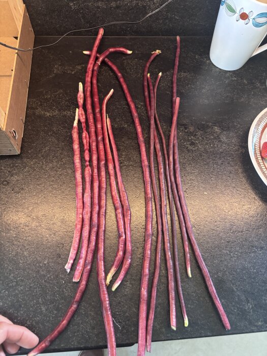 Långbönor ligger utspridda på ett mörkt bord, bredvid en mugg.