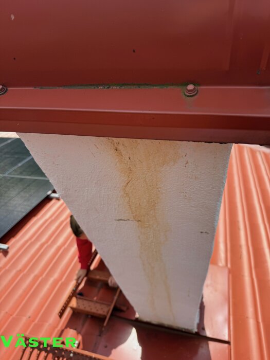 Fläckar av vattenläckage på vit murstock, med solpaneler och plåttak i bakgrunden. Orsak diskuteras i inlägg.