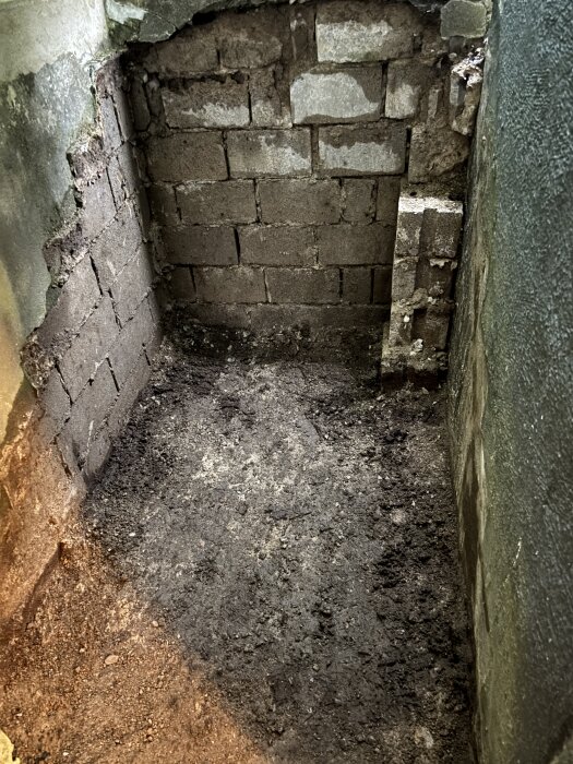 Tomt hålutrymme under gamla källartrappan, visar murade väggar och jordig botten, del av diskussion om material att fylla med.