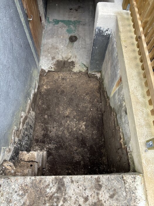 Källartrappa under renovering, visande marken där trappan ska gjutas. Källarmuren dränerad med pordrän, träformen delvis kvar. Fråga om fyllnadsmaterial.