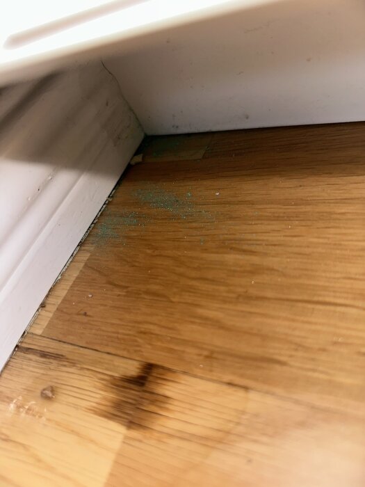 Golv med grönaktigt damm i ett gammalt hus, närbild av golvbrädor vid golvlist.