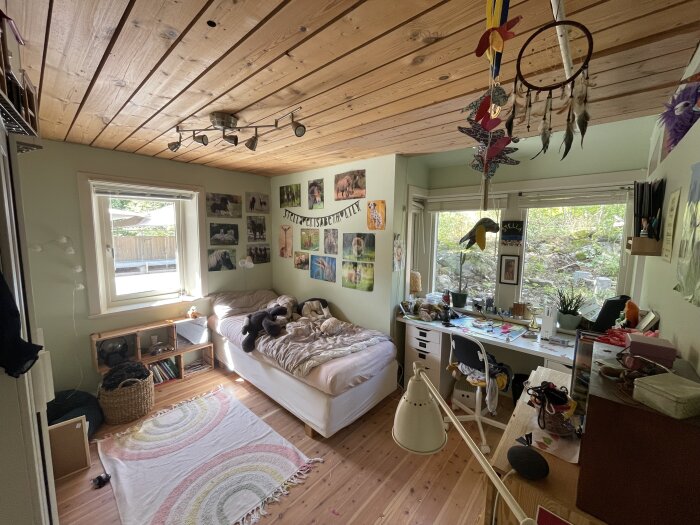 Barnrum med träpaneltak, grön vägg och fönster med ljusinsläpp. Säng och skrivbord med dekorationer och väggbilder.