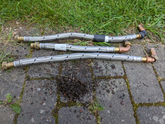 Tre flexslangar och en hög med sediment på stengång efter att ha bytts ut från en värmepump under underhåll.