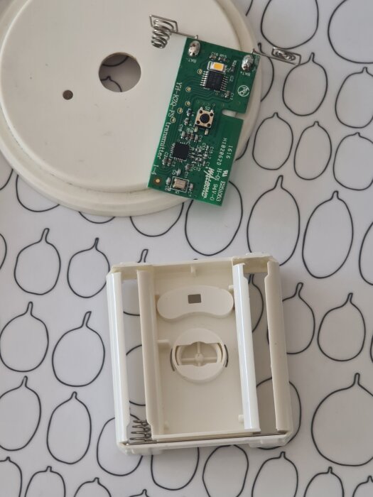 En isärplockad puck med kretskort och en brytare synlig, placerad på ett mönstrat underlag.