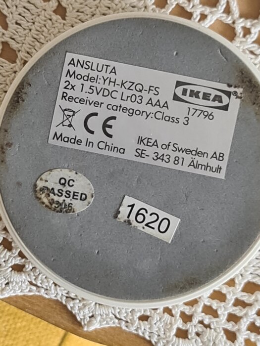 Baksida av en IKEA Ansluta puck, modell YH-KZQ-FS med specifikationer och etiketter, liggande på en virkad duk.