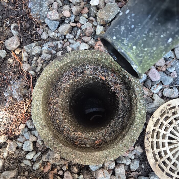 Stuprör över en brunn med grus runt, visar ett plaströr placerat snett inuti brunnen.